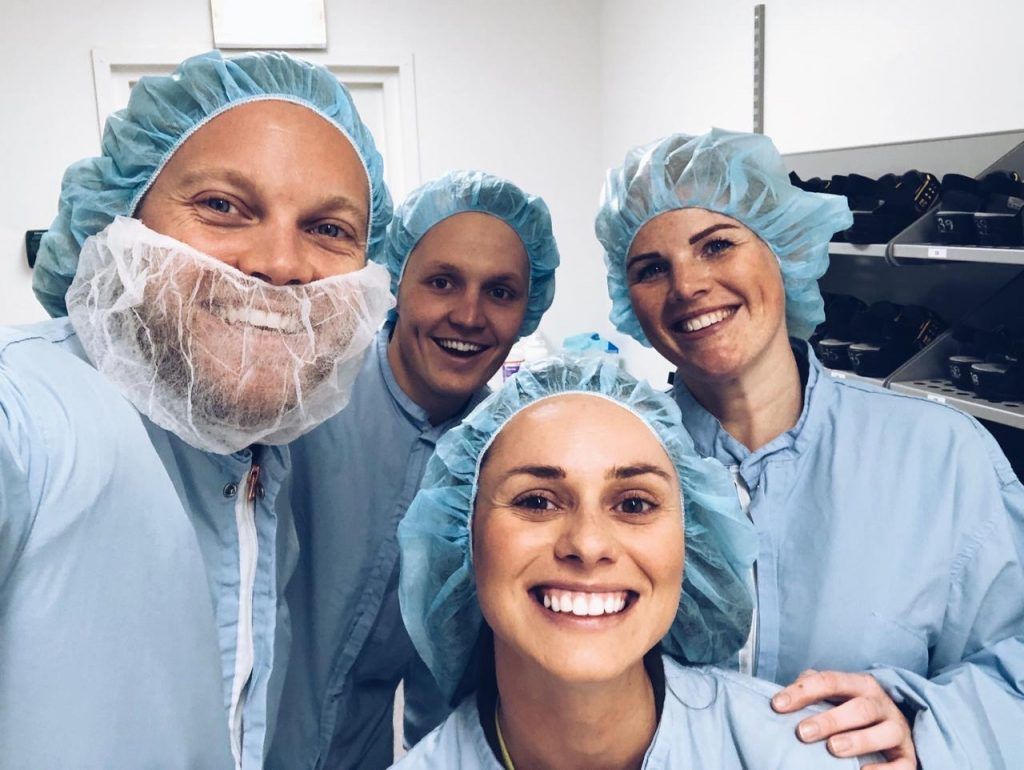 Gruppbild på nära håll av medarbetare på AztraZeneca och representater från Oddwork. Alla är klädda i ljusblå skyddskläder och skyddsmössor för håret.